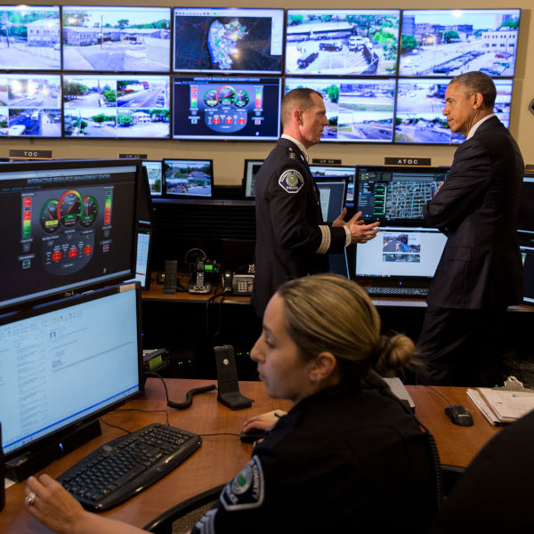 President Obama speaks to a police officer in a room full of computer monitors.