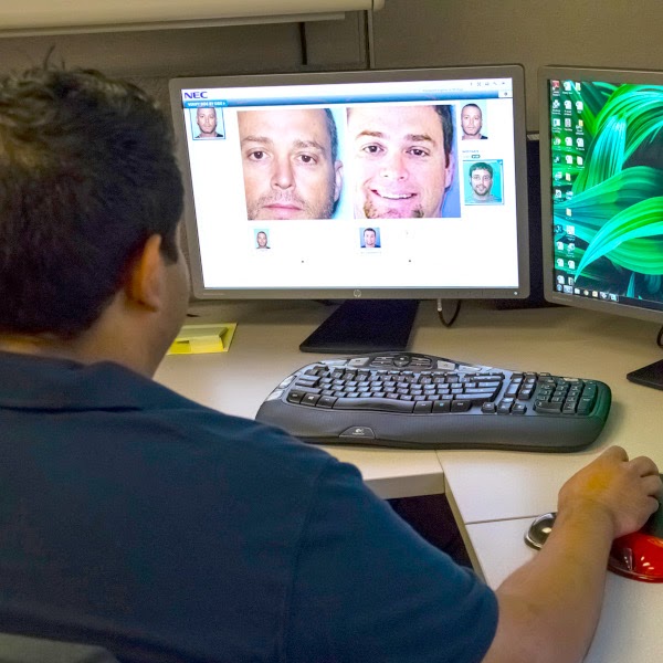 Back of man's head looking at computer monitor displaying face recognition software matching an image of a man's face
