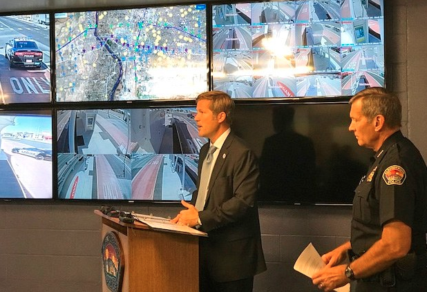 Albuquerque Mayor Tim Keller stands at a podium in front of a wall of monitors at the real-time crime center opening. 